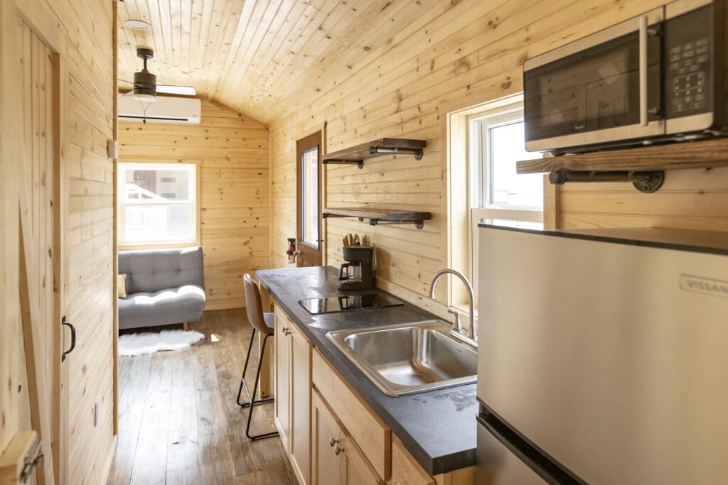 A view when living in a cabin that shows the wood paneling, kitchen sink, refrigerator, and more.